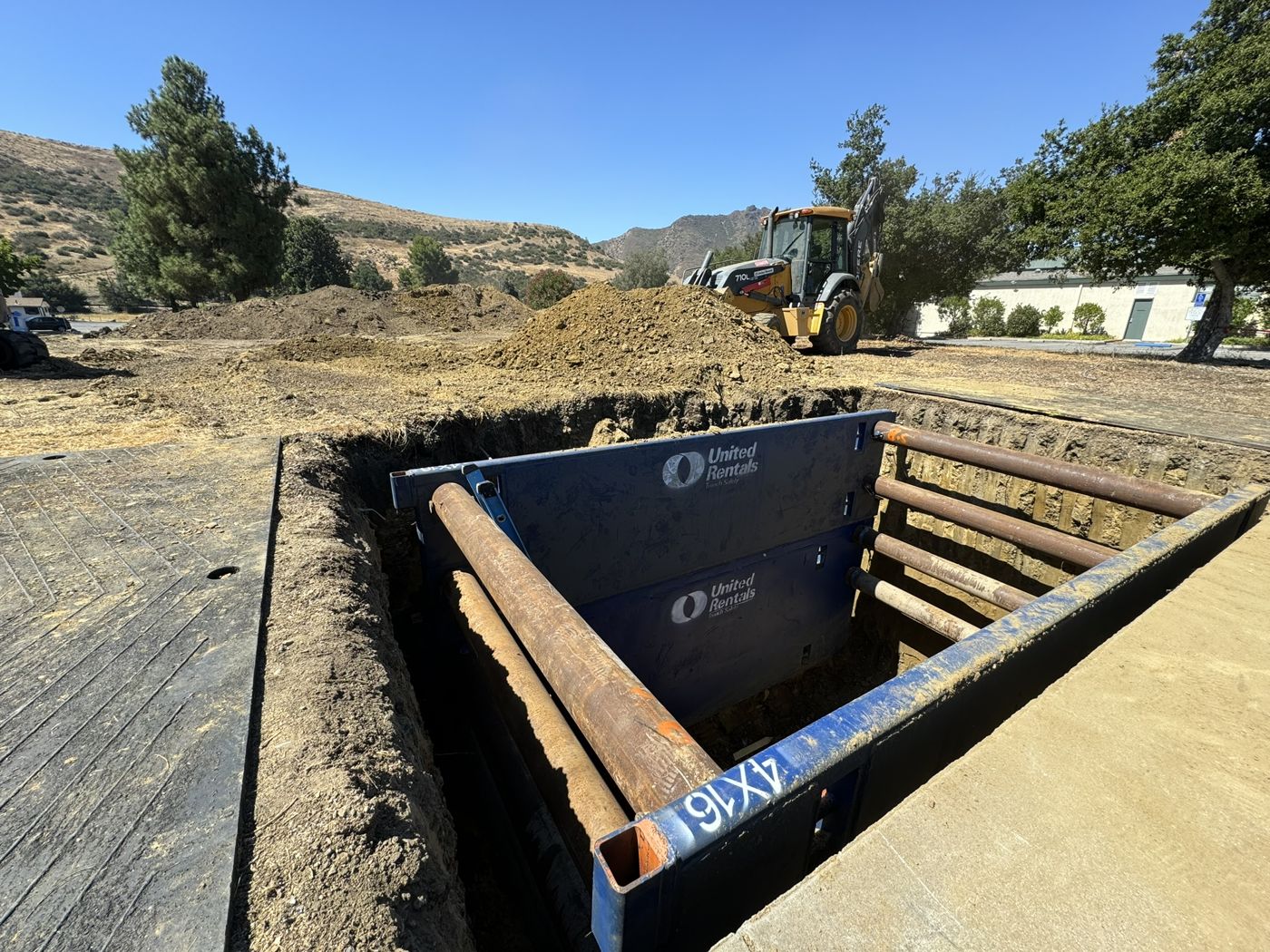 Deep trench shored with a trench box beside a backhoe